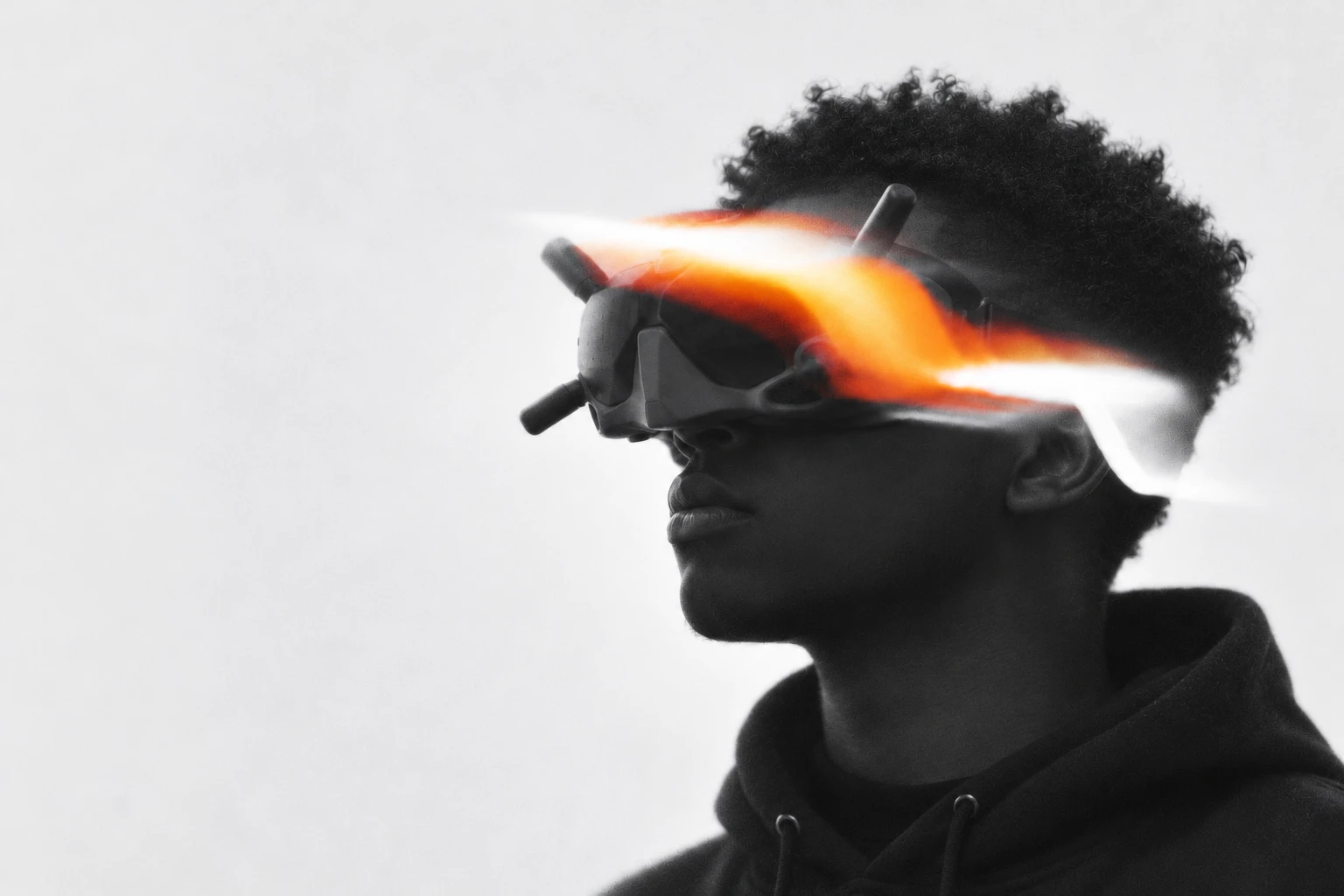 Dera wearing DJI FPV goggles, in monochrome with an orange light trail.